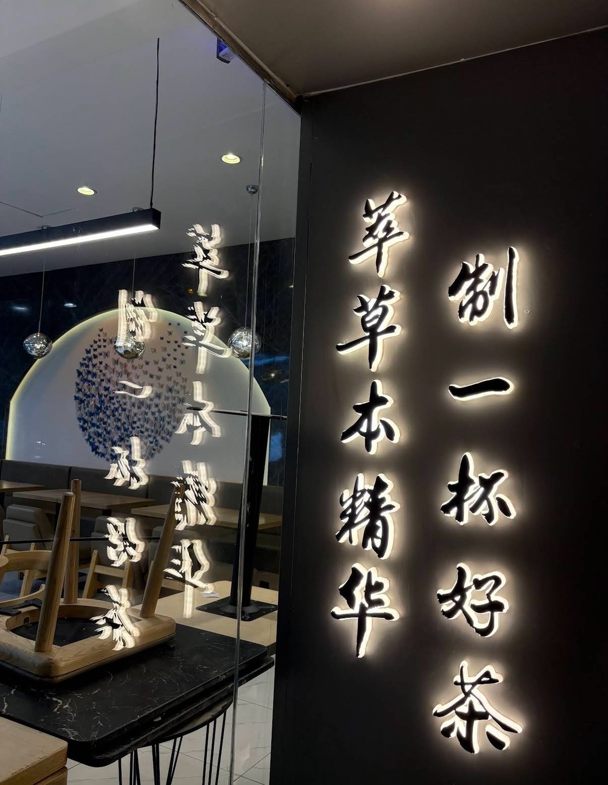 店内暗色背景墙上的中文书法灯箱，写着「萃草本精华 制一杯好茶」，暖白光勾勒字形