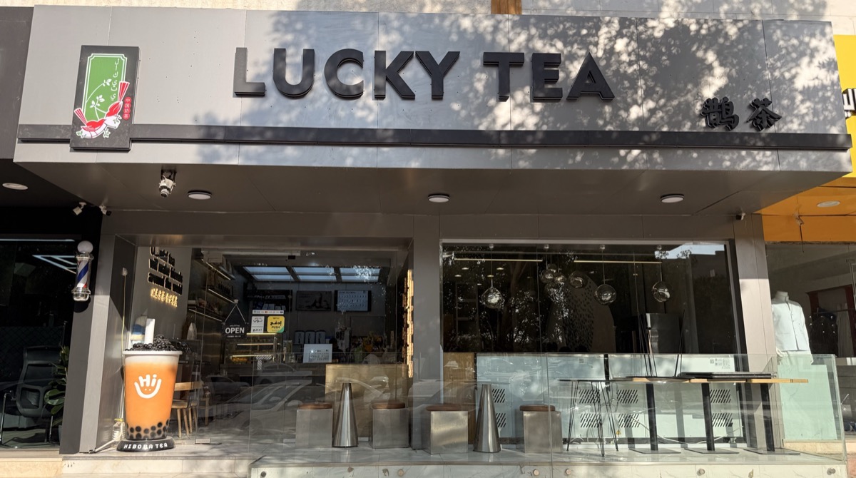 鹊茶哈马达尼街门店招牌与店面，紧邻街边一家理发店入口