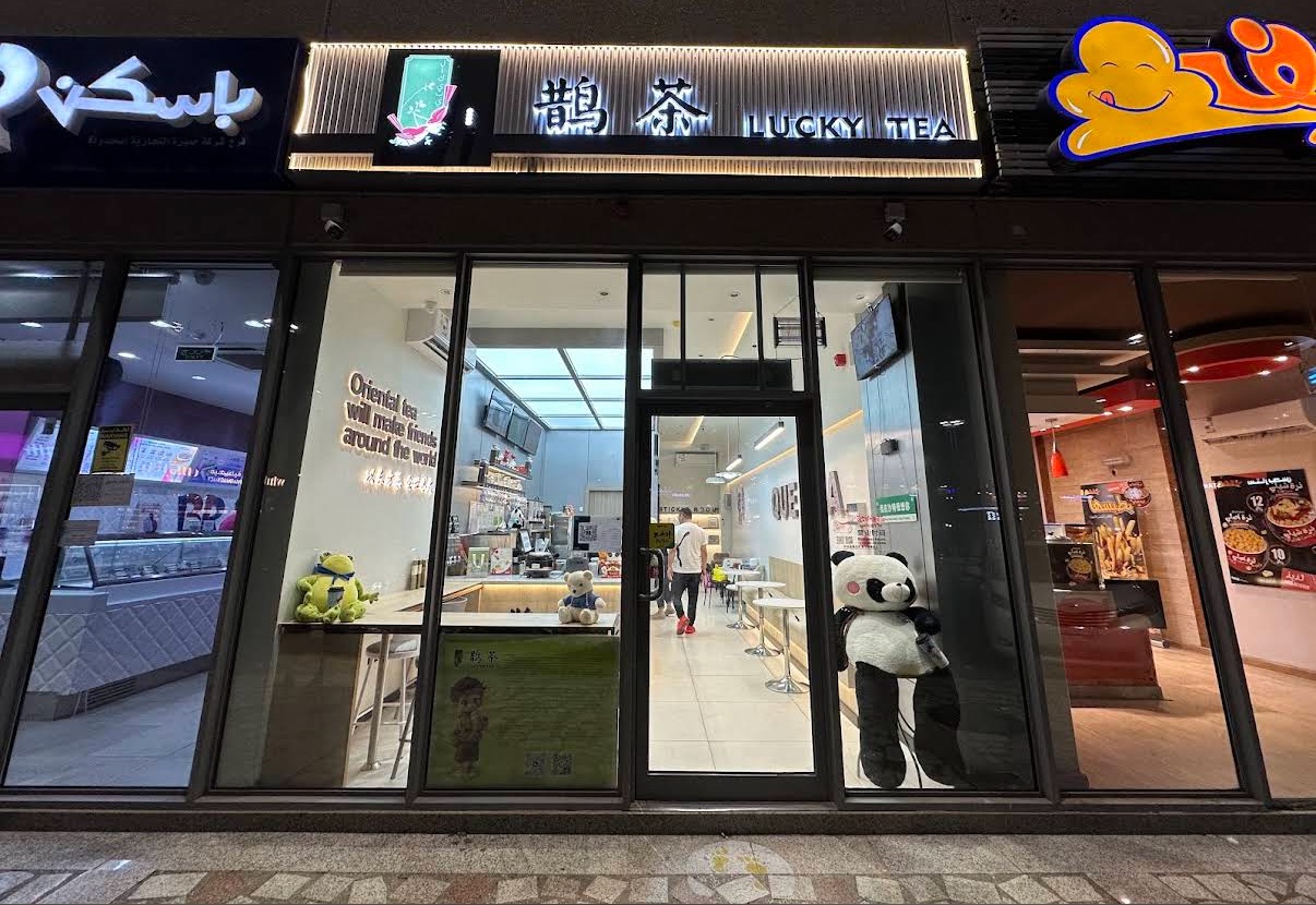 鹊茶哈姆拉店夜间店面灯光通明，橱窗里摆着毛绒玩偶，店内墙上写着「以东方茶会世界友」