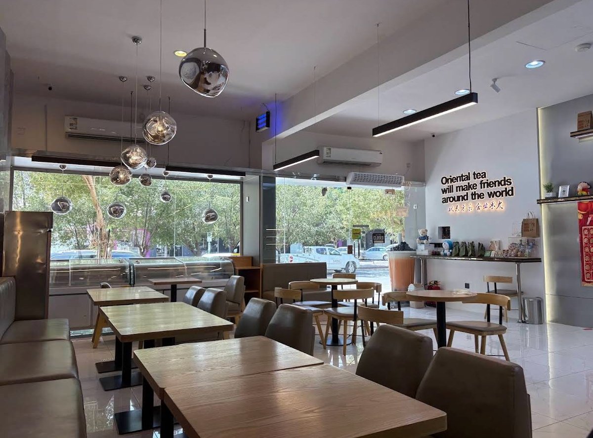 Bright interior seating area at a Lucky Tea cafe in Riyadh, with wood tables, pendant lights, and greenery visible through the windows