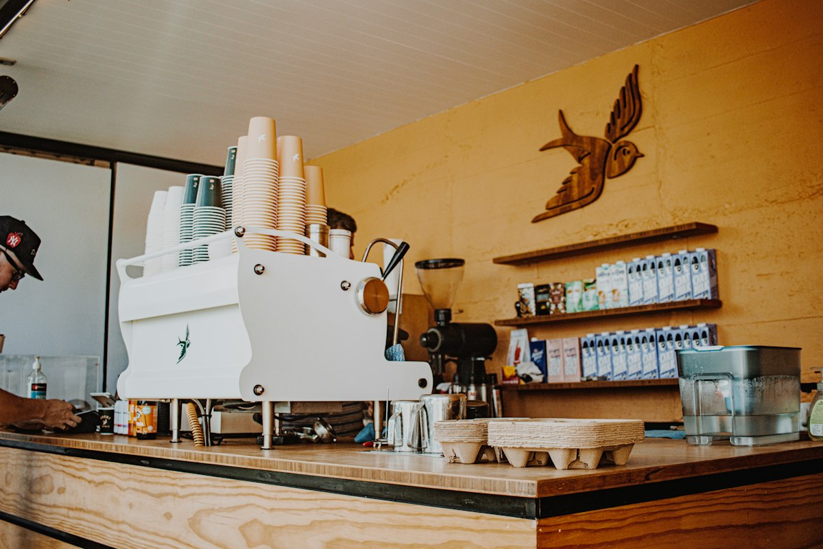An espresso machine and stacked paper cups on a cafe counter, evoking tea shops adding coffee service to diversify revenue